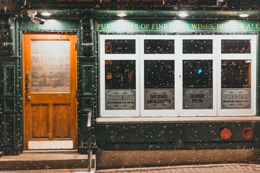 Cozy Irish pub entrance with Christmas lights and snowfall creating a warm evening scene.