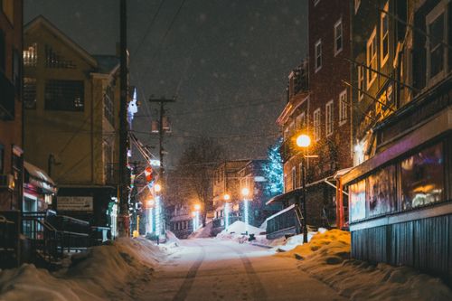 Free A serene urban street at night during snowfall, illuminated by street lamps. Stock Photo