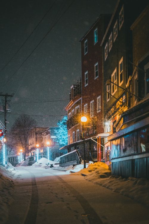 Free A tranquil night scene on a snowy town street lit by warm street lamps and holiday lights. Stock Photo