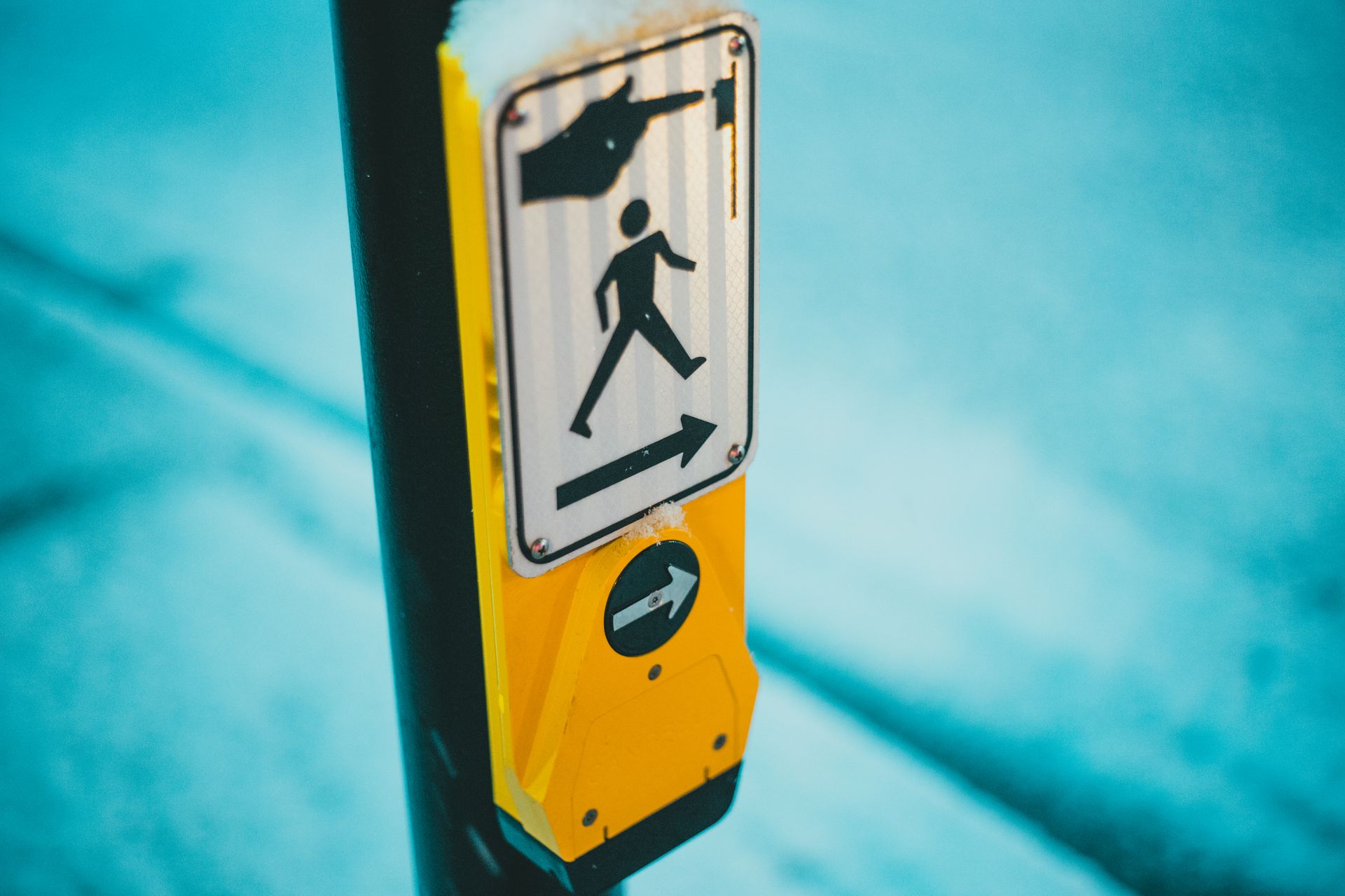Selective focus of blind and deaf friendly pedestrian crosswalk control button for changing traffic lights and crossing street on zebra in traffic with sign on street