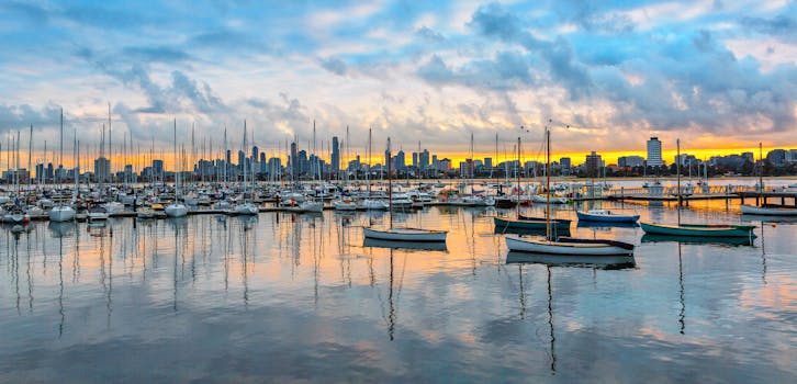 A stunning view of a marina with numerous sailboats and a vibrant city skyline at sunset.