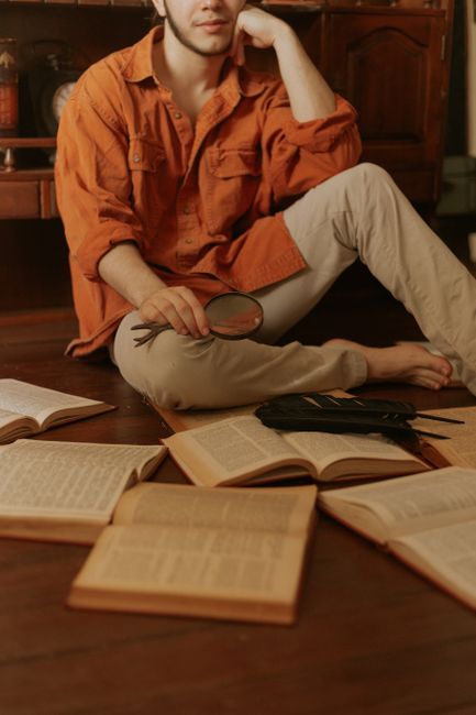 A man studies with a magnifying glass and open books in a cozy indoor setting, promoting education and learning.
