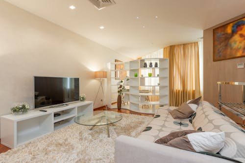 Glass round coffee table placed on soft fur rug between comfortable sofa and modern TV set in spacious living room