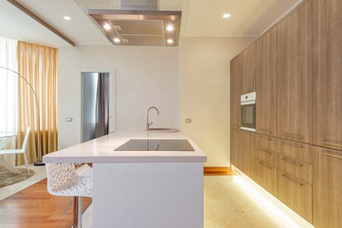 Kitchen island counter with built in stove and sink near big wooden cabinets and dining area in modern apartment