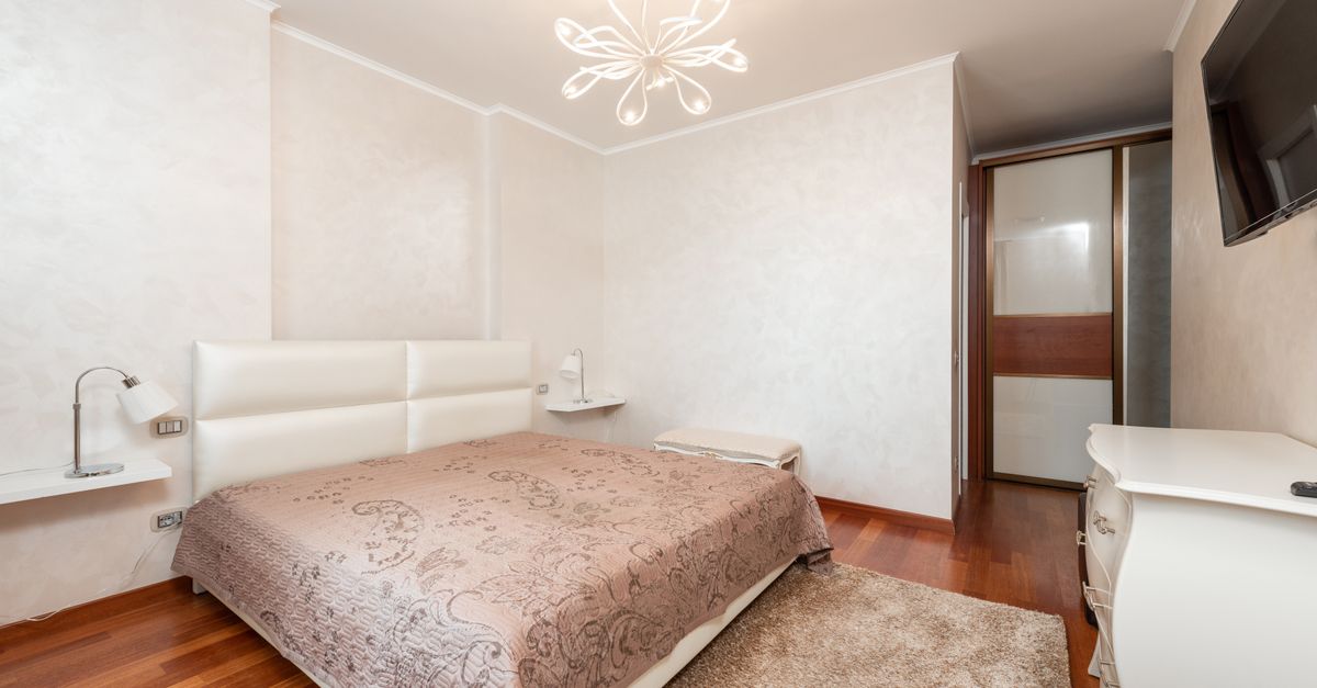 Interior of spacious bedroom with comfortable bed and modern TV hanging on wall above classic styled white commode