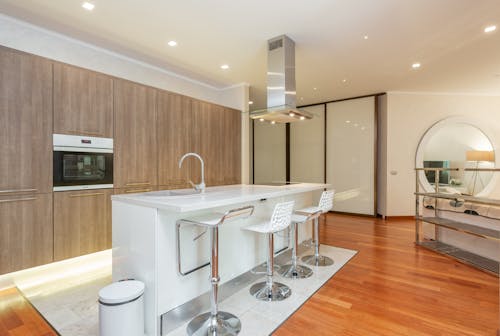 Chairs placed near white counter near wooden cupboards with built in oven in spacious modern studio apartment with kitchen and living room