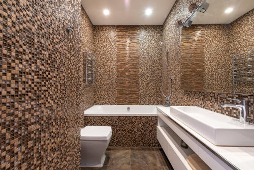 Mosaic tiled walls in modern bathroom with ceramic sink on white cabinet and bathtub