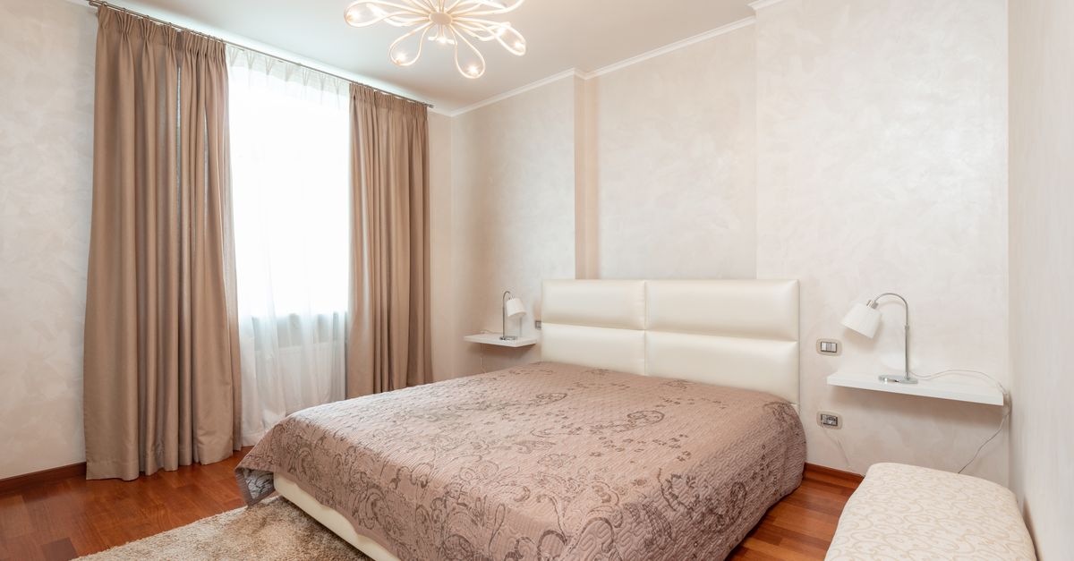 Comfortable bed with coverlet in cozy bedroom decorated with chandelier and lamps in classic styled apartment