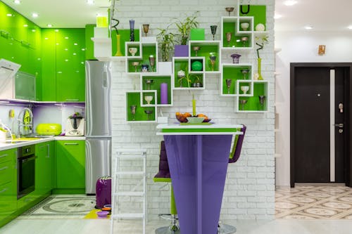 Free Creative shelves decorated with various vases and plants hanging on white brick wall above counter in contemporary kitchen with bright green and purple furniture Stock Photo