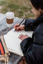 Crop Asian student drawing in notebook at table in park