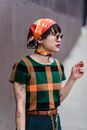 Stylish young ethnic female in checkered t shirt and sunglasses with cigarette looking away on urban pavement
