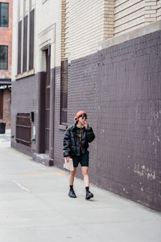 A young woman in stylish casual wear smokes while walking on a city sidewalk.