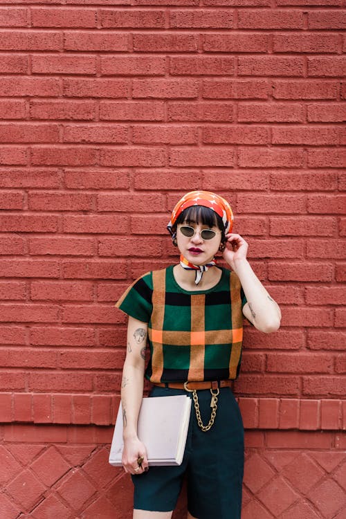 Trendy Asian student in sunglasses against brick wall