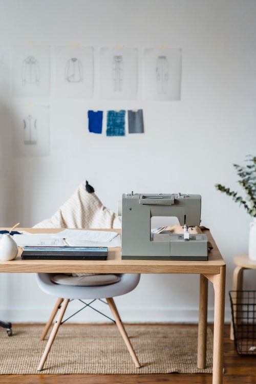 Free Professional sewing machine on wooden table near chair at wall with drafts of clothes and samples of textile in atelier Stock Photo