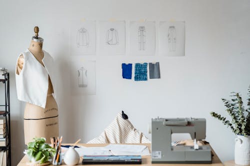 Free Table with sewing machine placed near mannequin with garment at white wall with drafts of cloth and samples of textile Stock Photo