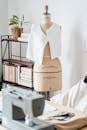Table with professional sewing machine placed near mannequin with white cloth near wall in light modern atelier with collection of books