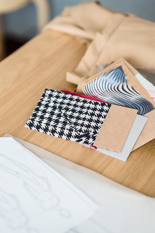 From above samples of colorful fabric placed on wooden table with brown cloth and sketches on paper in light modern atelier