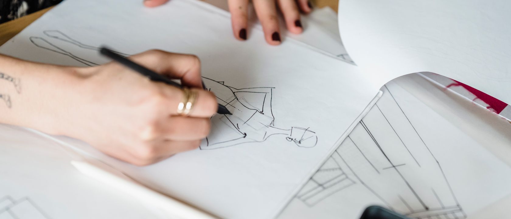 From above of crop anonymous female designer drawing draft of stylish garment at table with papers in modern light workshop