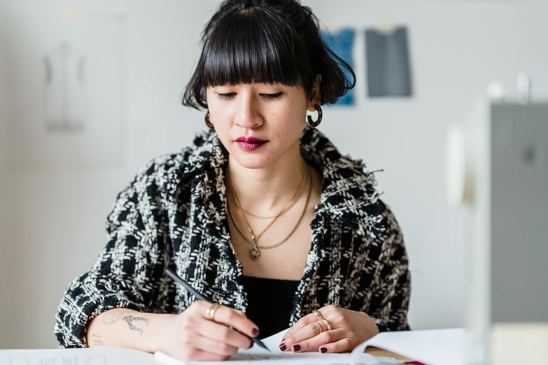 Asian female drawing on paper while working on clothing design on blurred background