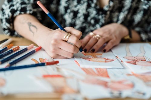 Free Crop anonymous tattooed female designer coloring apparel illustration on human figure on paper sheet while working at desk Stock Photo