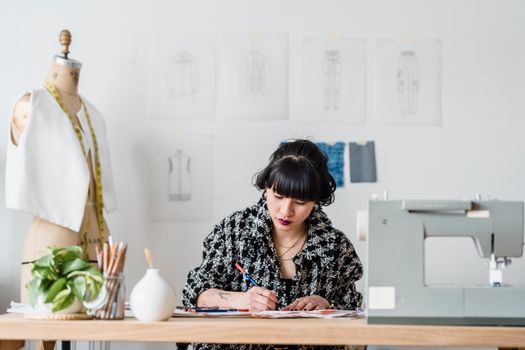 Attentive Asian designer coloring illustration at desk in atelier