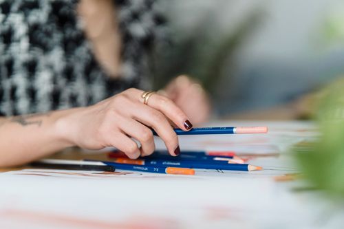Free Crop anonymous tattooed female illustrator with collection of colored pencils and paper illustrations at home desk Stock Photo