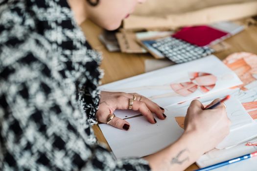 Side view of crop anonymous tattooed female designer with pencil coloring illustration of wear on human figure at desk