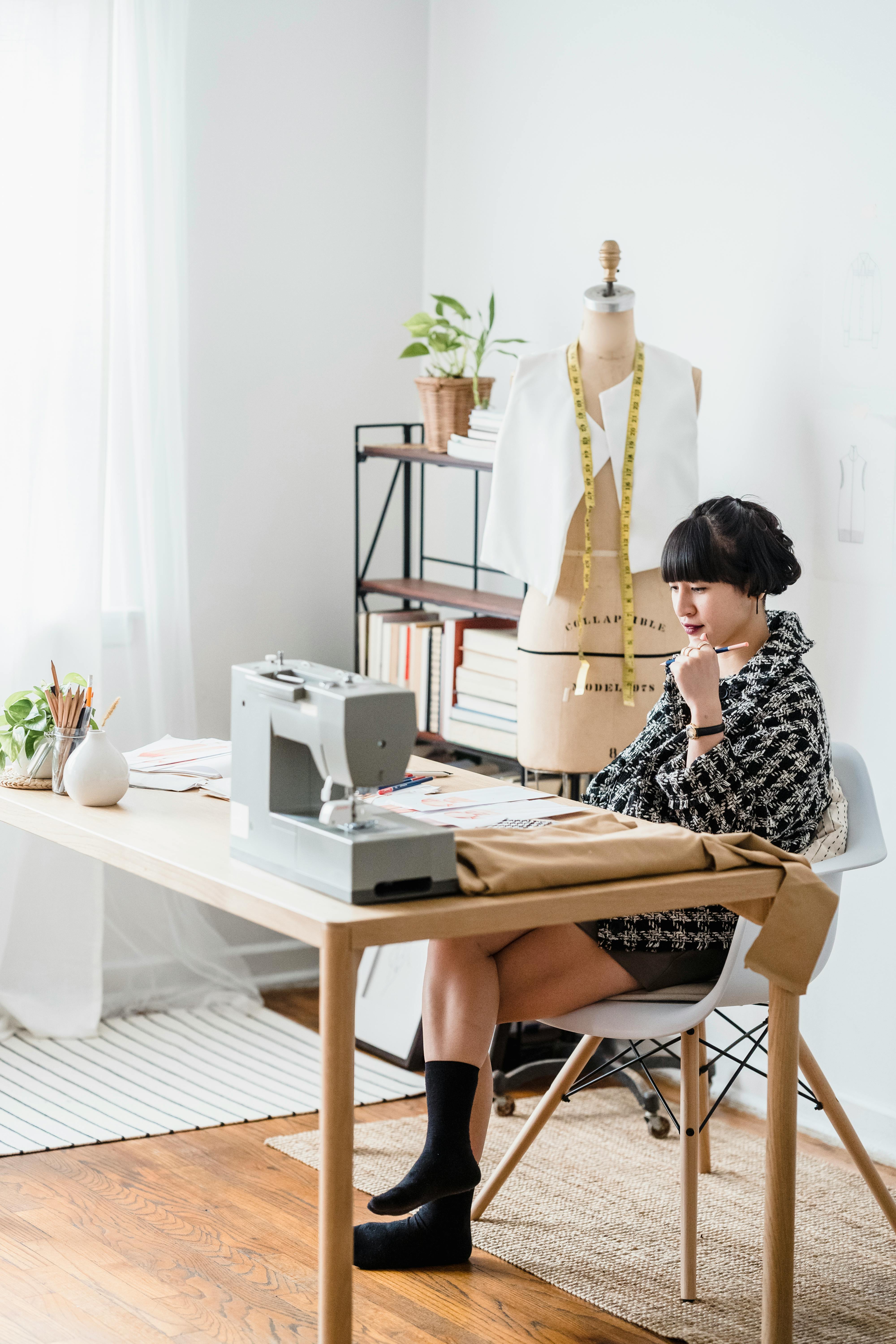 thoughtful asian designer at table with illustrations in workshop