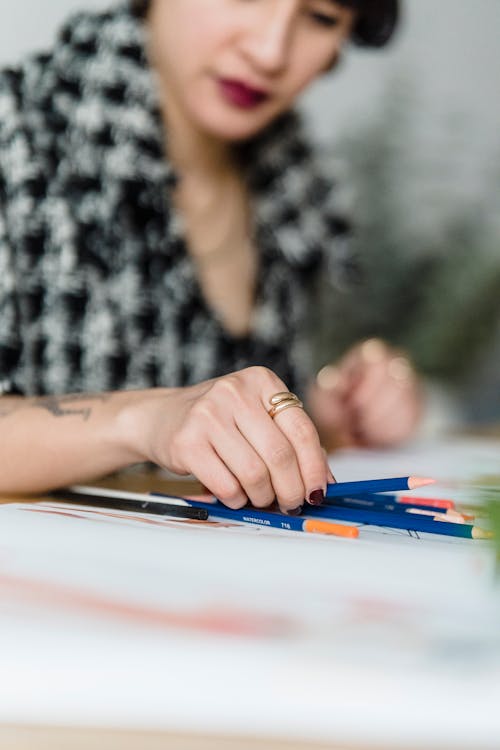 Crop ethnic designer choosing pencil at table with papers