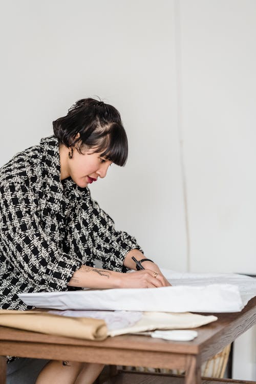 Free Focused Asian designer drawing on paper at table in workroom Stock Photo