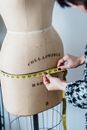 Crop unrecognizable female dressmaker with flexible ruler measuring hip line of dummy while working in studio
