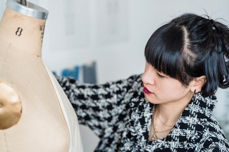 Focused Asian Dressmaker Trying Cloth On Dummy In Atelier