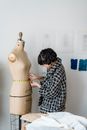 Side view of female tailor in checkered outfit measuring waist of dummy with flexible ruler in atelier