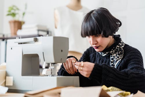 Focused Asian tailor threading sewing machine in workshop