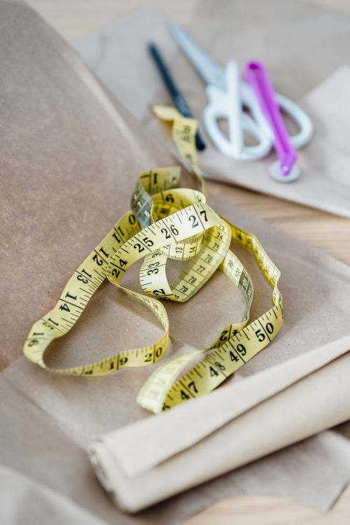 Free From above of yellow measuring tape placed on craft paper on table with scissor and pens in modern light atelier Stock Photo