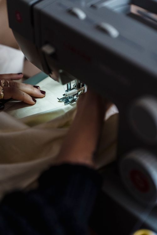 Free Crop anonymous skilled tailor with manicure sewing white fabric on professional sewing machine while working in atelier with modern equipment Stock Photo
