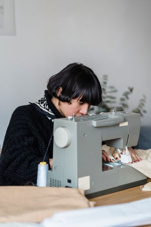 Free Side view of concentrated Asian female tailor using sewing machine while working at table with fabric in modern light studio Stock Photo
