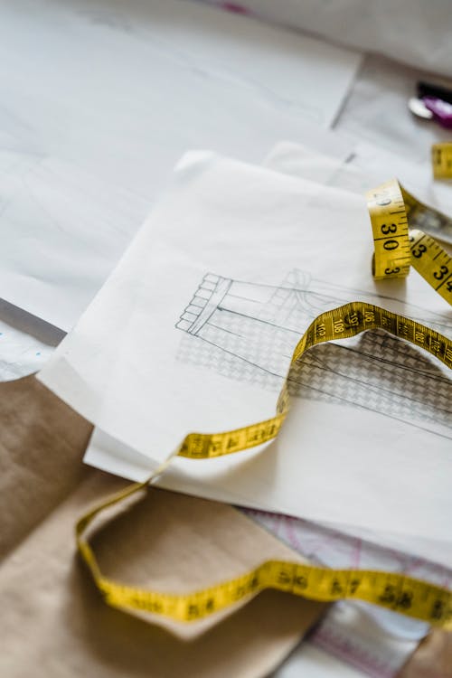 From above of measuring tape on white paper with draft of modern garment placed on table with craft paper in atelier