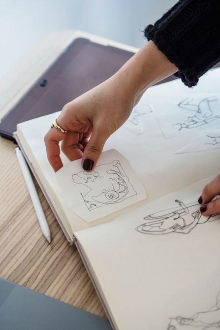 Fotomural Una mujer examina bocetos de moda en un escritorio, mostrando creatividad en un estudio de diseño.