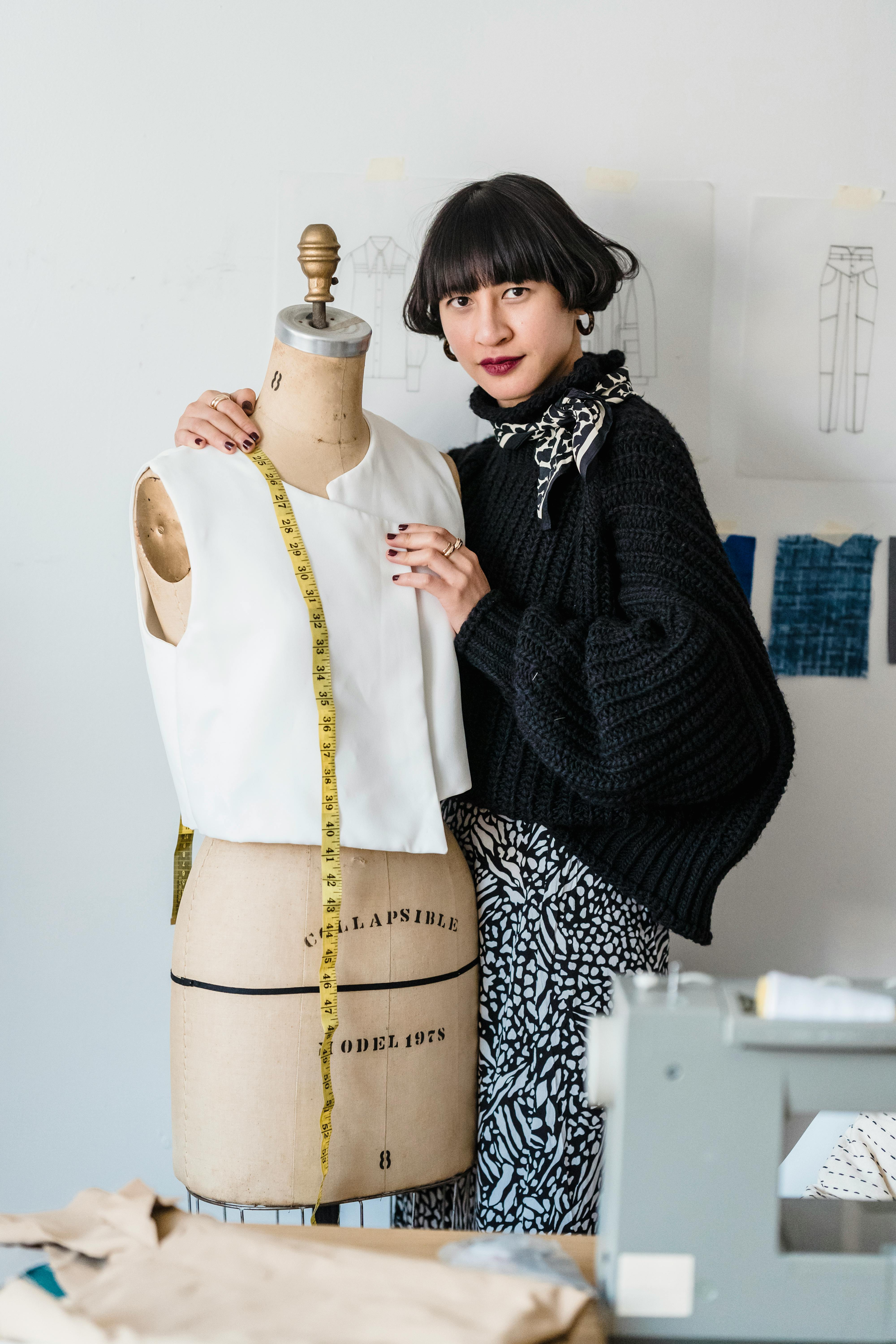 stylish young ethnic fashion designer measuring mannequin in workshop