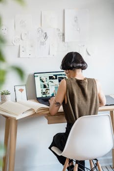 A young creative designer working remotely at her desk with sketches and a laptop.