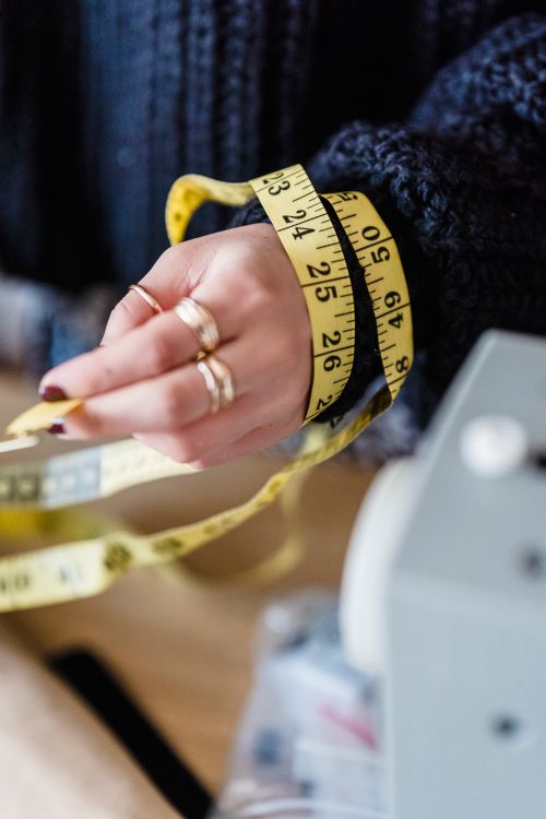 Free From above of crop unrecognizable female with yellow measuring tape preparing for sewing on blurred background Stock Photo