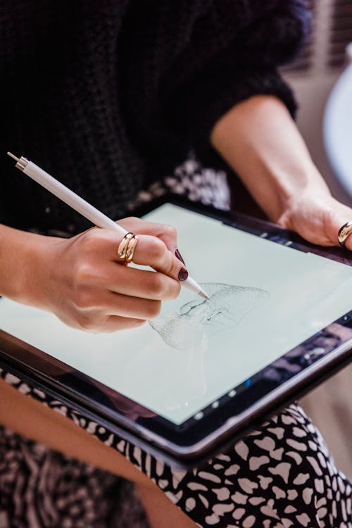 Crop unrecognizable female making sketch of face on contemporary graphic tablet on blurred background in daylight