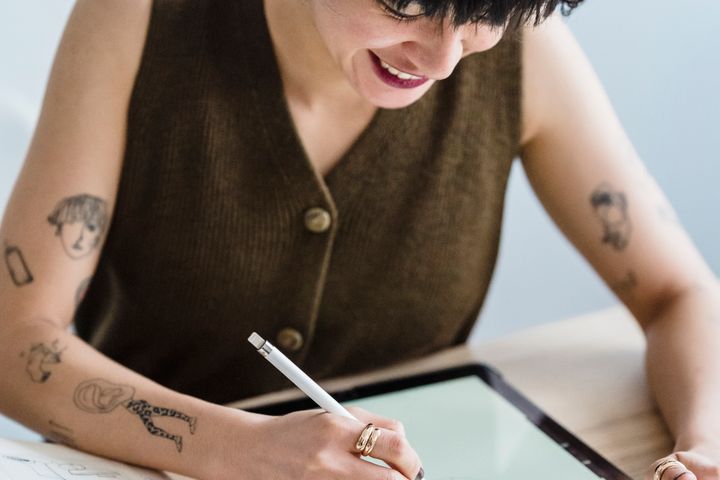 Smiling woman drawing on graphic tablet with pencil at table