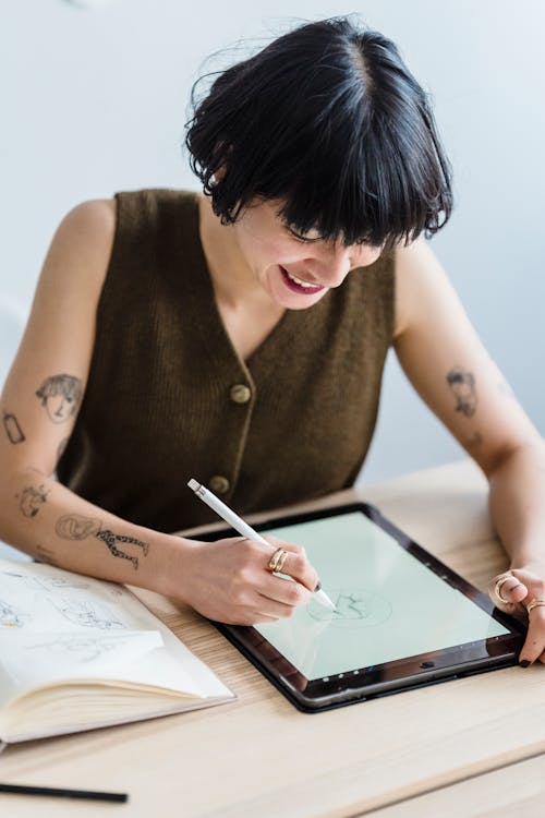 Smiling woman drawing on graphic tablet with pencil at table