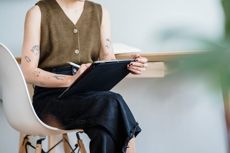 Crop Woman Drawing In Tablet While Sitting On White Chair