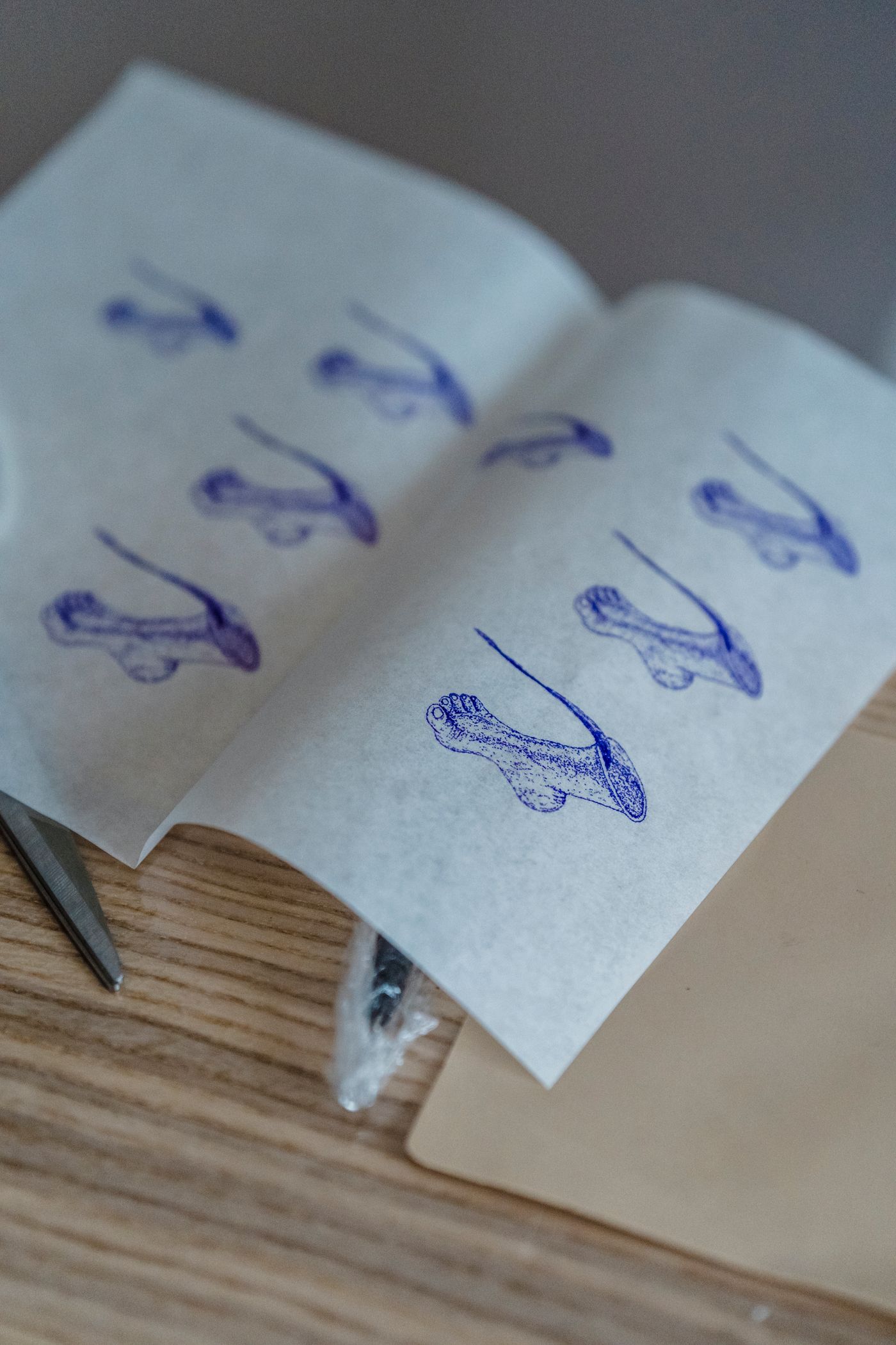 Blue-ink tattoo design impressions on white sheets beside tattooing tools on a worktable.