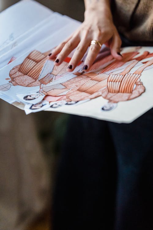 Crop dressmaker with folder of fashion illustrations in workshop