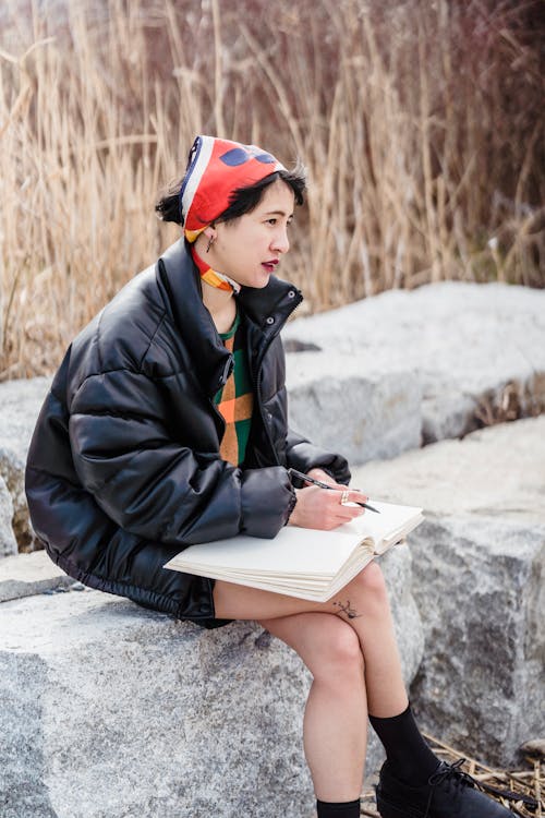 Asian female sitting on stone and writing notes in notebook in nature