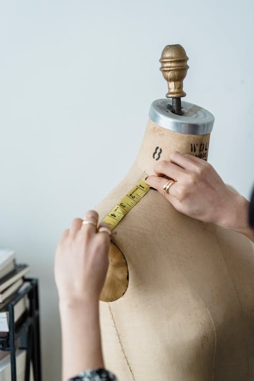 Free Crop unrecognizable seamstress measuring shoulder of mannequin against light wall in atelier in daytime Stock Photo